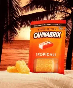 Cannabis-infused gummies by Cannabrix, Tropicali flavor, on sandy beach at sunset with palm trees.