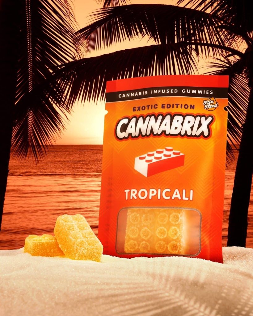 Cannabis-infused gummies by Cannabrix, Tropicali flavor, on sandy beach at sunset with palm trees.