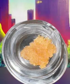 Golden cannabis concentrate in a clear jar against a colorful cityscape background.